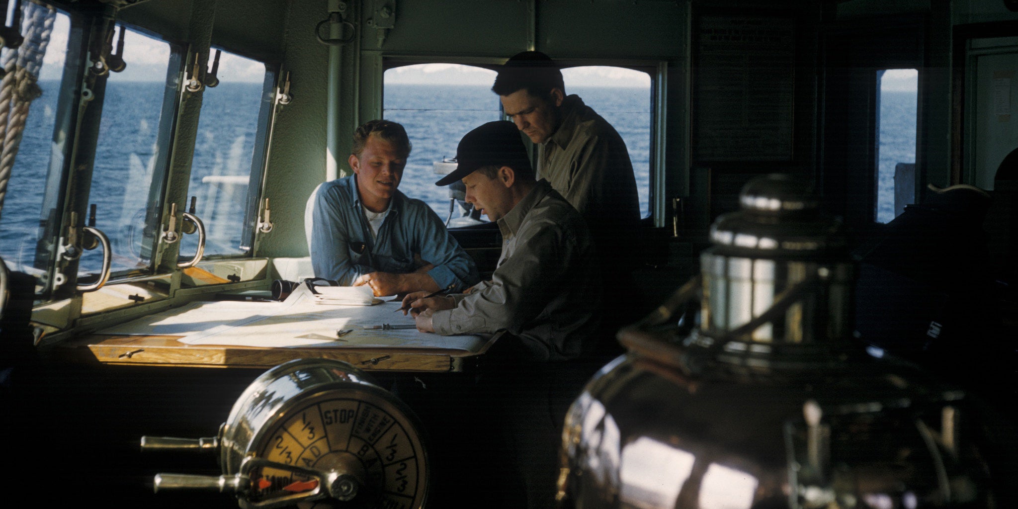 Crew members having a toolbox meeting in navigation bridge. Engine telegraph showing half ahead